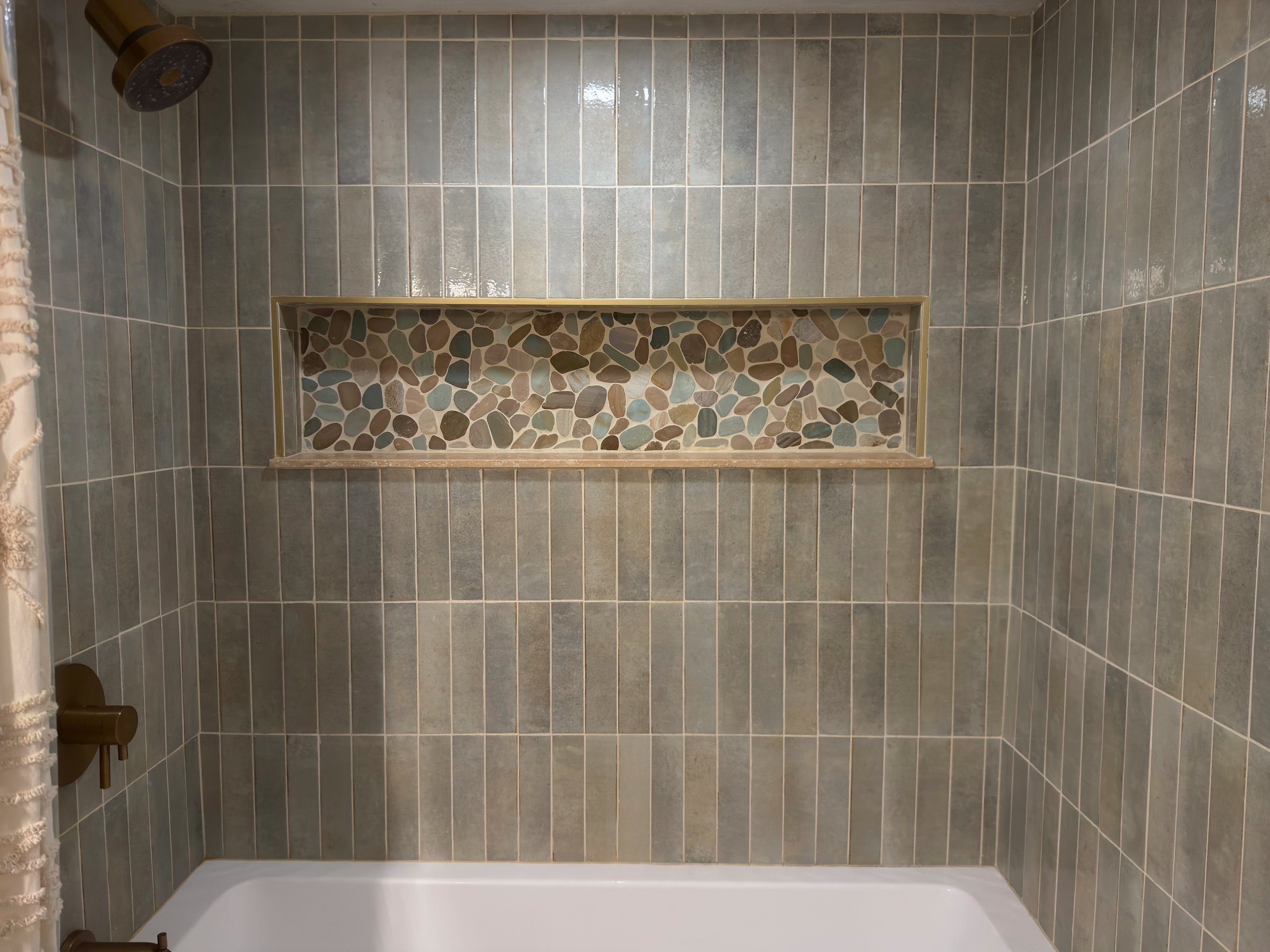 Finished shower with vertical gray tile and a pebble mosaic niche